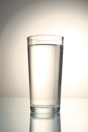 Photo of Fresh water in glass on mirror table against gray gradient background