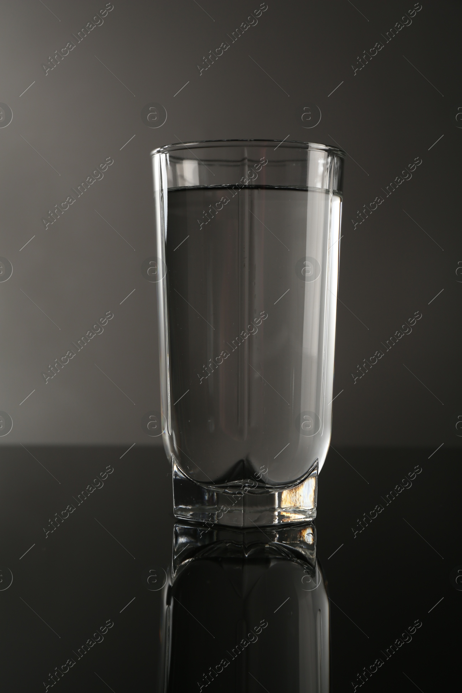 Photo of Fresh water in glass on mirror table against gray background