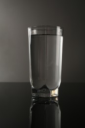 Photo of Fresh water in glass on mirror table against gray background