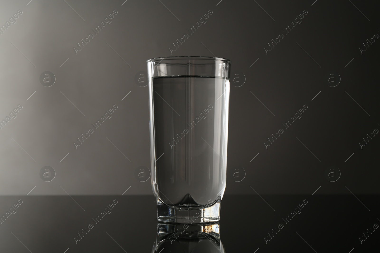 Photo of Fresh water in glass on mirror table against gray background