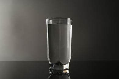 Photo of Fresh water in glass on mirror table against gray background