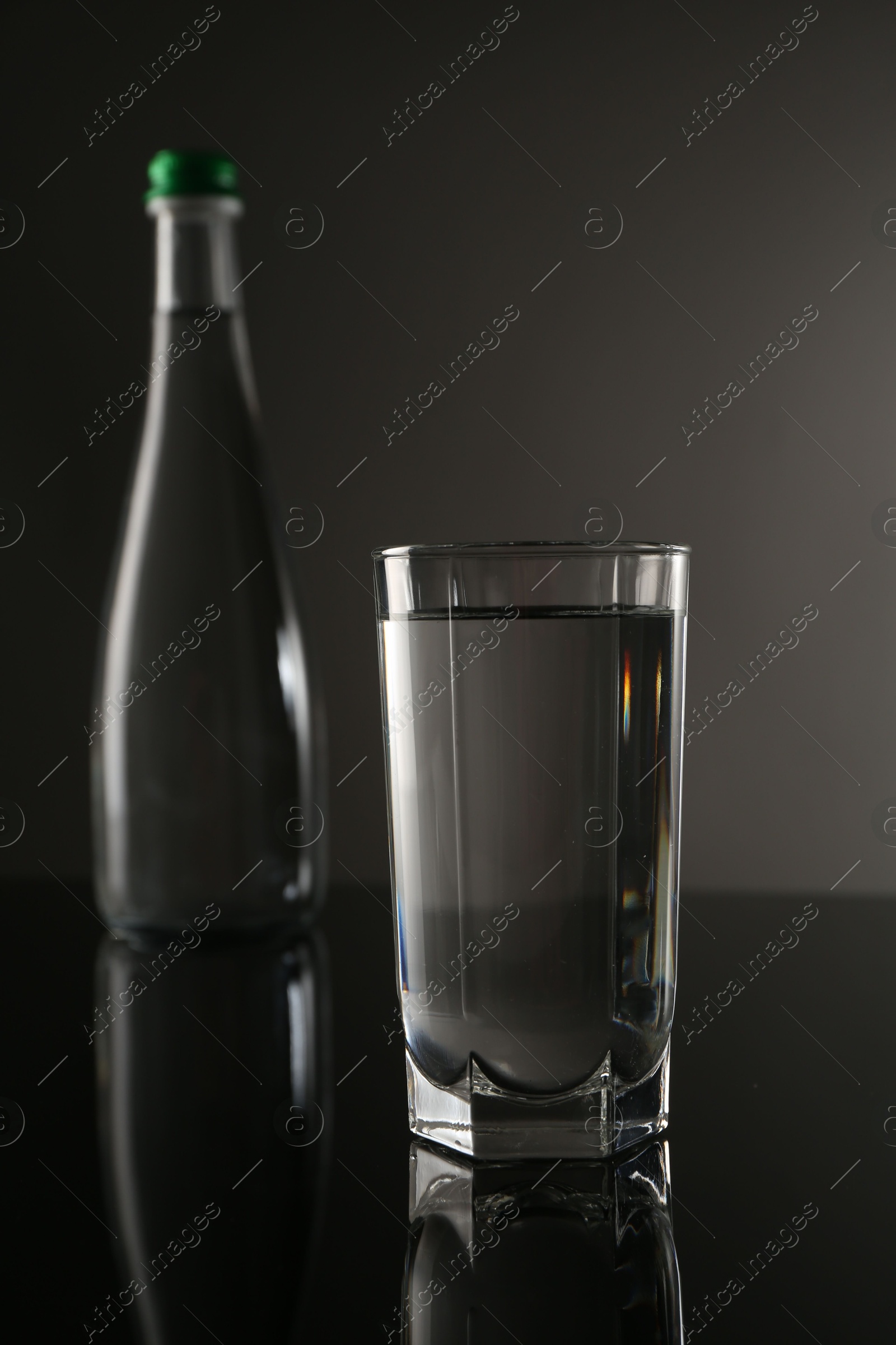 Photo of Fresh water in glass and bottle on mirror table against gray background, selective focus