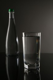 Photo of Fresh water in glass and bottle on mirror table against gray background, selective focus