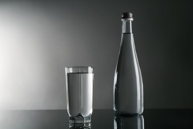 Photo of Fresh water in glass and bottle on mirror table against gray background