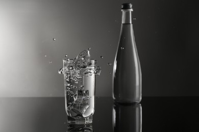Photo of Fresh water splashing out of glass on mirror table against gray background