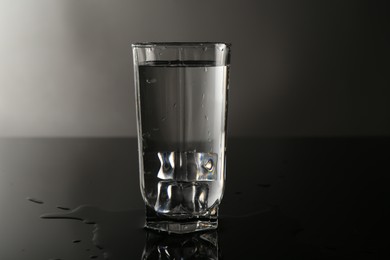 Photo of Fresh water with ice cubes in glass on mirror table against gray background