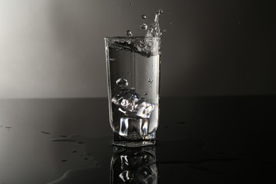 Photo of Fresh water splashing out of glass on mirror table against gray background