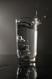 Photo of Fresh water splashing out of glass on mirror table against gray background