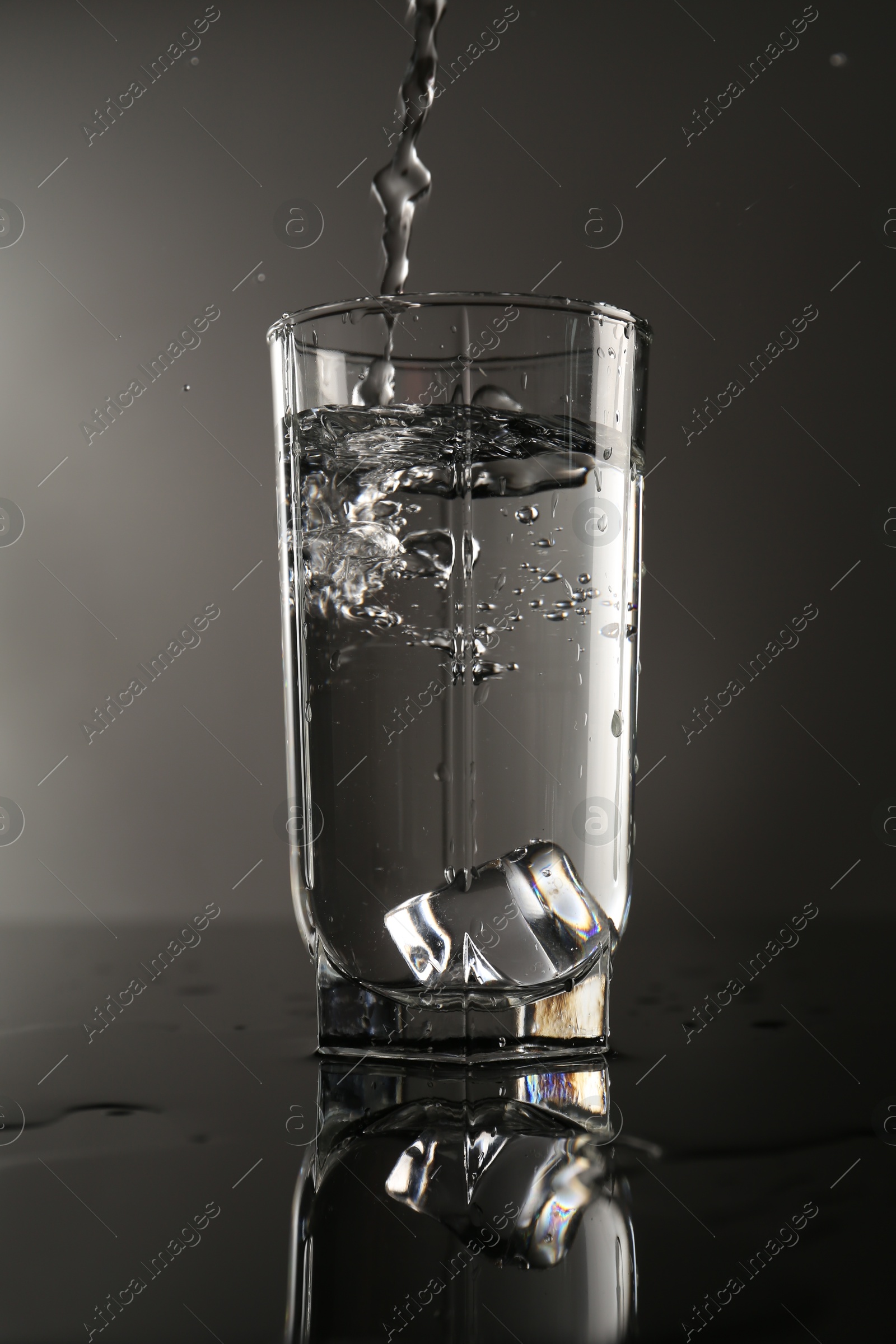 Fresh water splashing out of glass on mirror table against gray background Photo of Fresh water splashing out of glass on mirror table against gray background