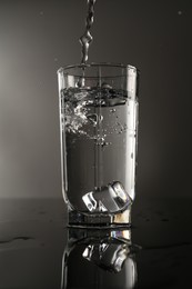 Photo of Fresh water splashing out of glass on mirror table against gray background