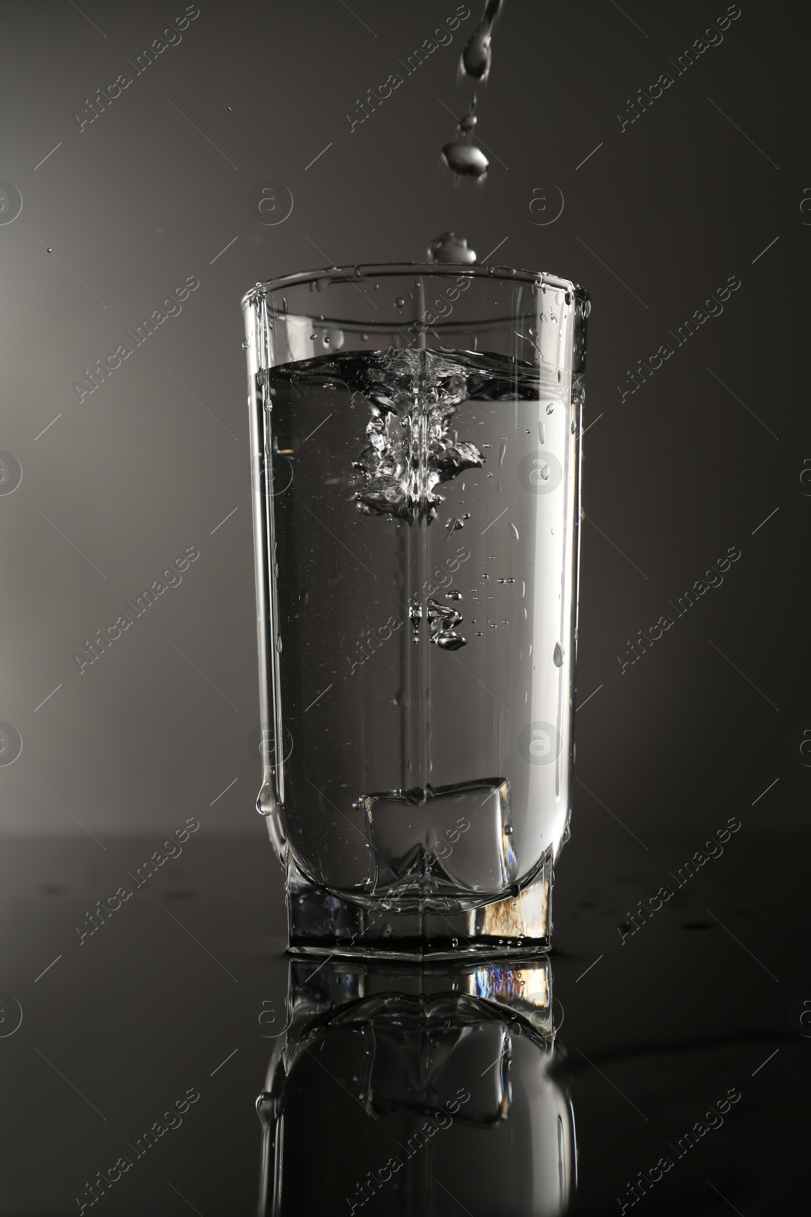 Fresh water splashing out of glass on mirror table against gray background Photo of Fresh water splashing out of glass on mirror table against gray background