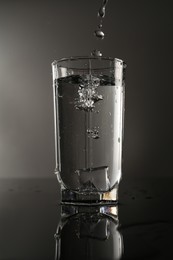 Photo of Fresh water splashing out of glass on mirror table against gray background