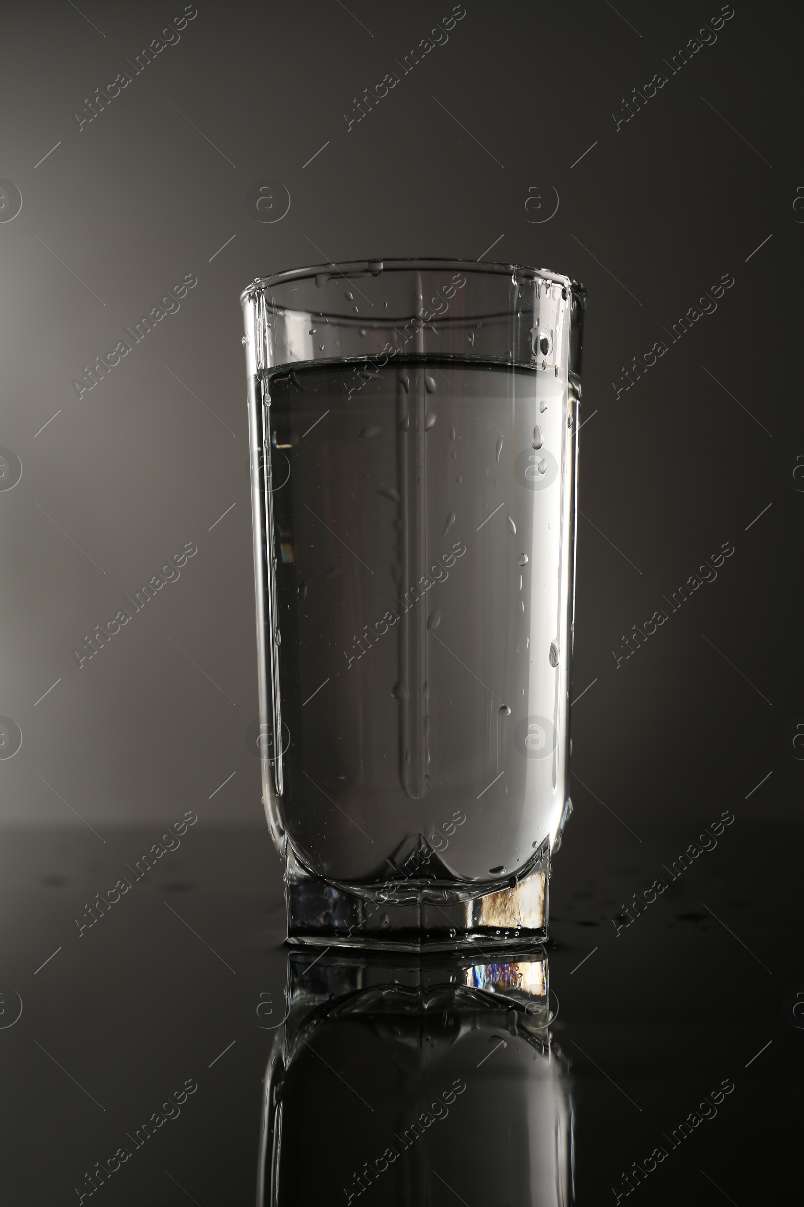 Fresh water in glass on mirror table against gray background Photo of Fresh water in glass on mirror table against gray background