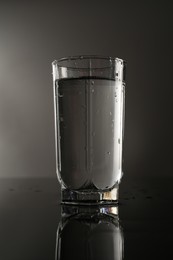 Photo of Fresh water in glass on mirror table against gray background