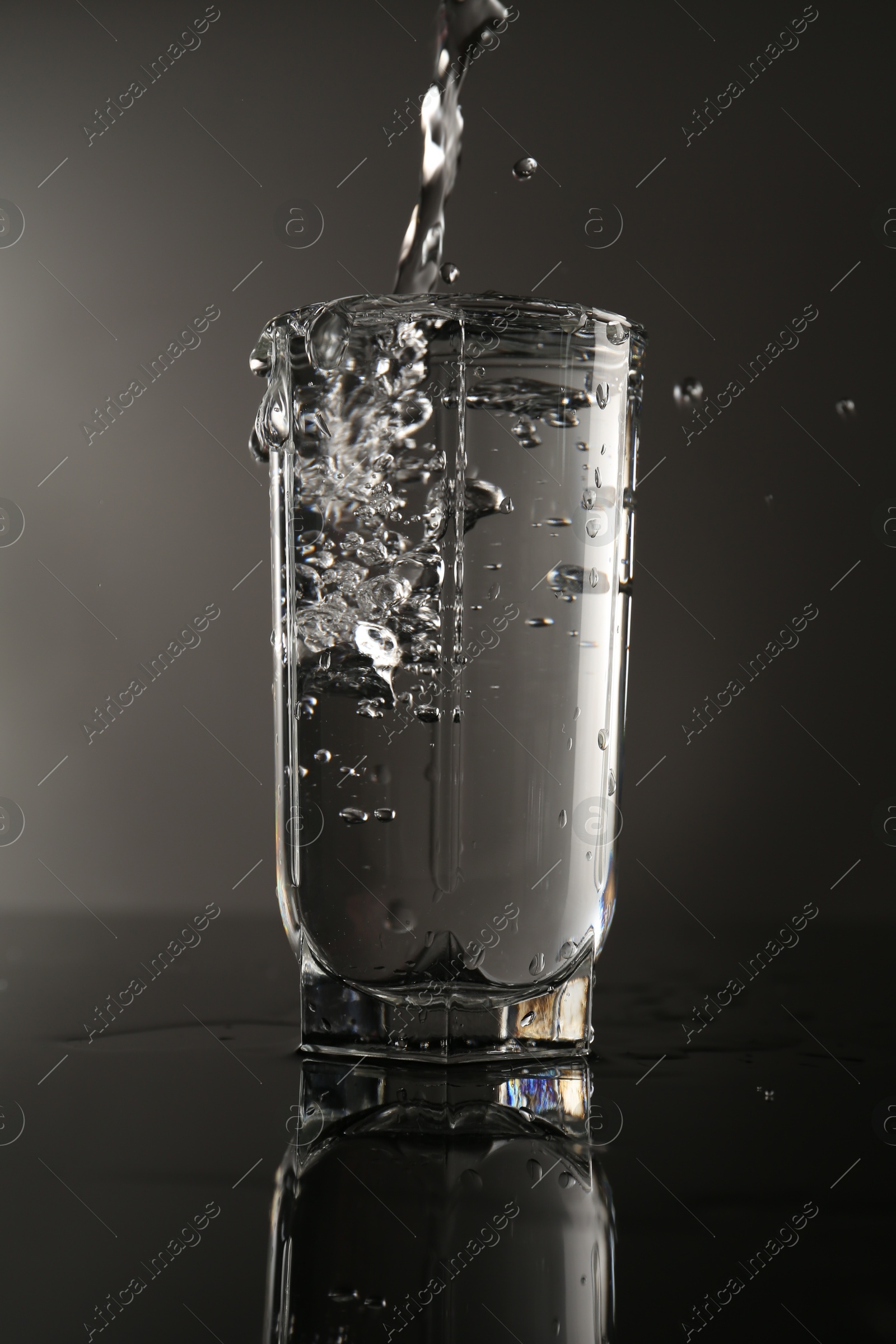 Fresh water splashing out of glass on mirror table against gray background Photo of Fresh water splashing out of glass on mirror table against gray background
