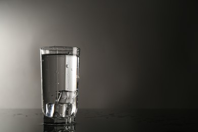 Photo of Fresh water with ice cubes in glass on mirror table against gray background, space for text