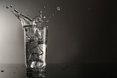 Photo of Fresh water splashing out of glass on mirror table against gray background, space for text