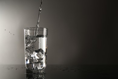 Photo of Pouring water into glass on mirror table against gray background, space for text