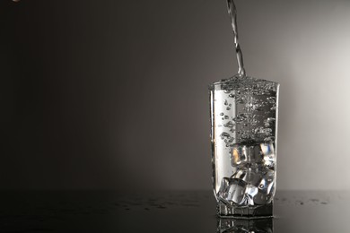 Photo of Pouring water into glass on mirror table against gray background, space for text