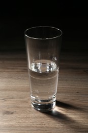 Photo of Fresh water in glass on wooden table against dark background