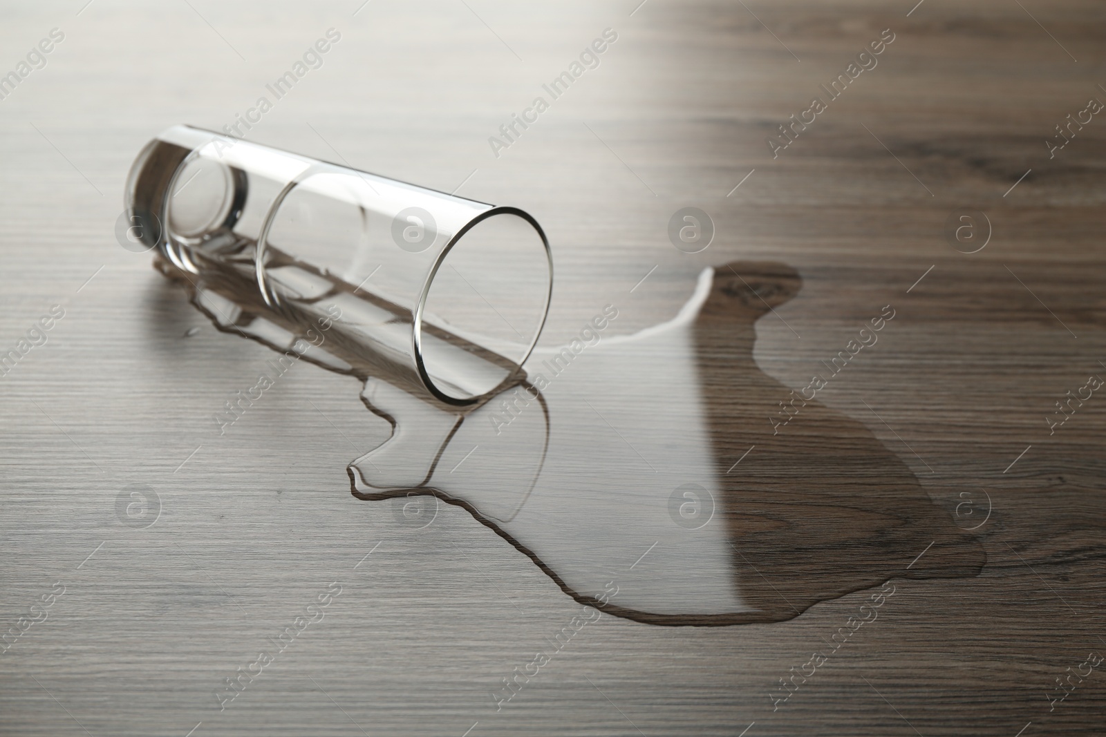 Overturned glass and spilled water on wooden table Photo of Overturned glass and spilled water on wooden table