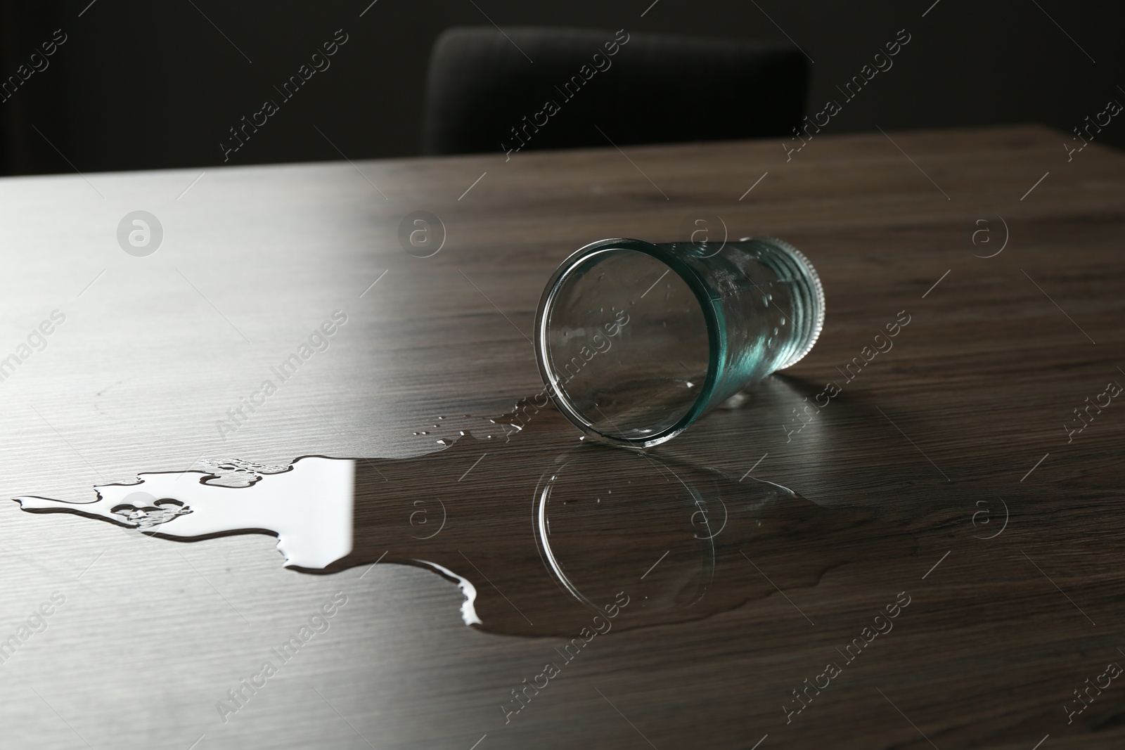 Overturned glass and spilled water on wooden table Photo of Overturned glass and spilled water on wooden table