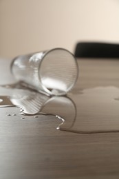 Photo of Overturned glass and spilled water on wooden table, selective focus