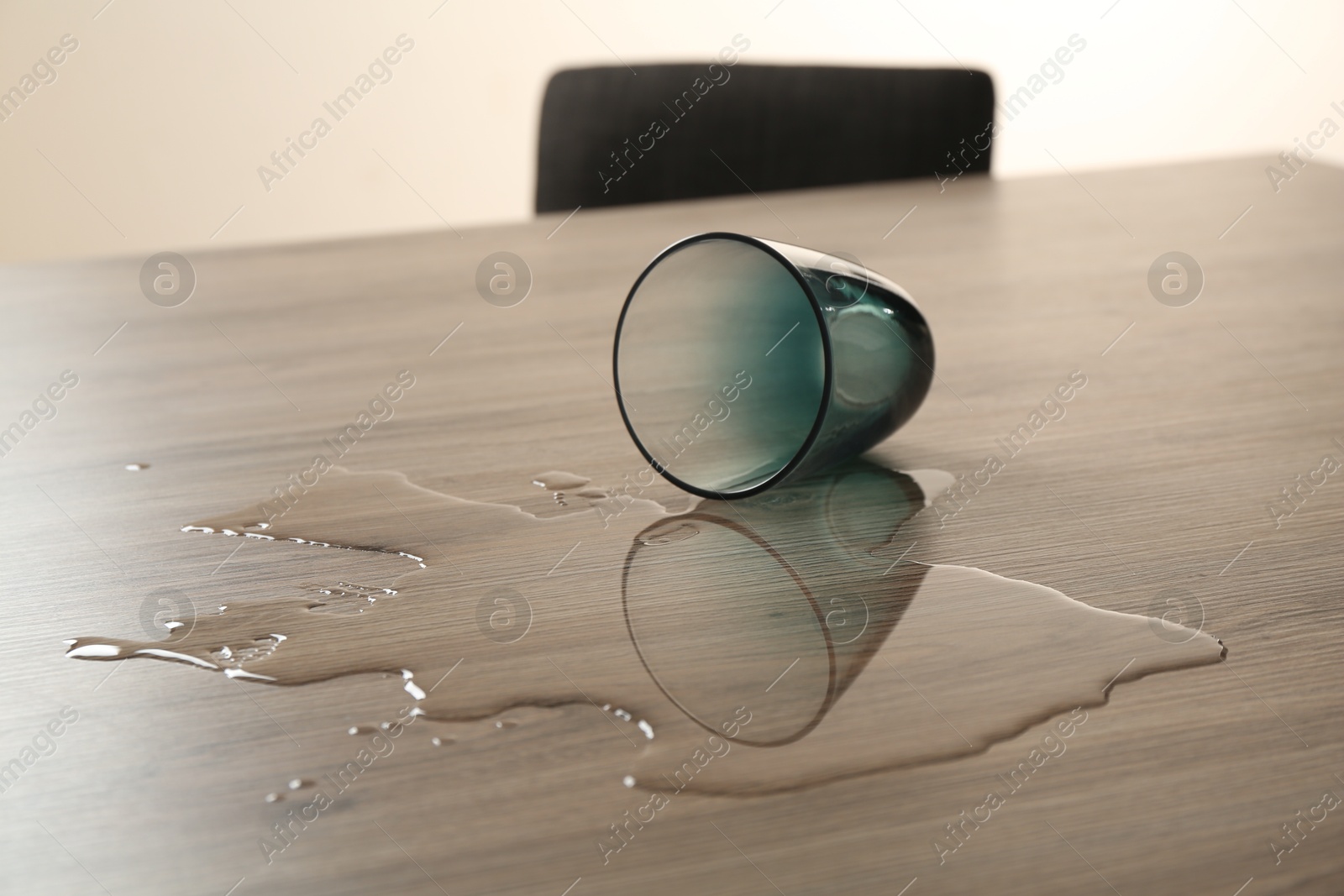 Overturned glass and spilled water on wooden table Photo of Overturned glass and spilled water on wooden table