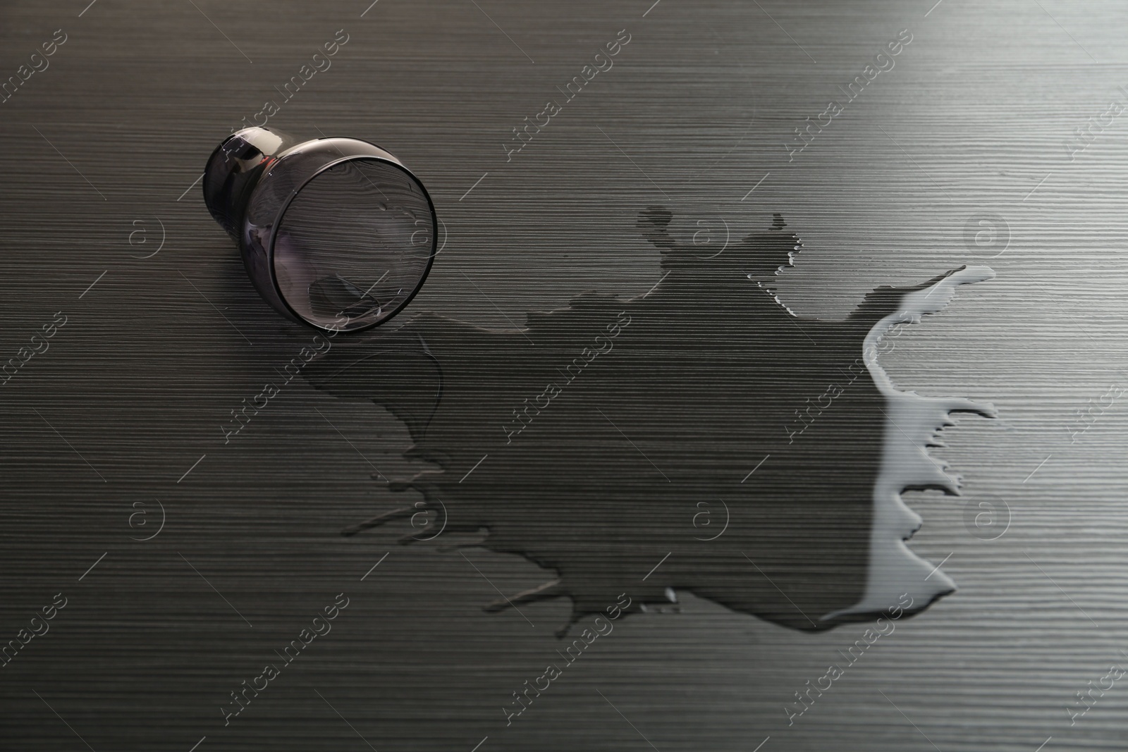 Overturned glass and spilled water on wooden table Photo of Overturned glass and spilled water on wooden table