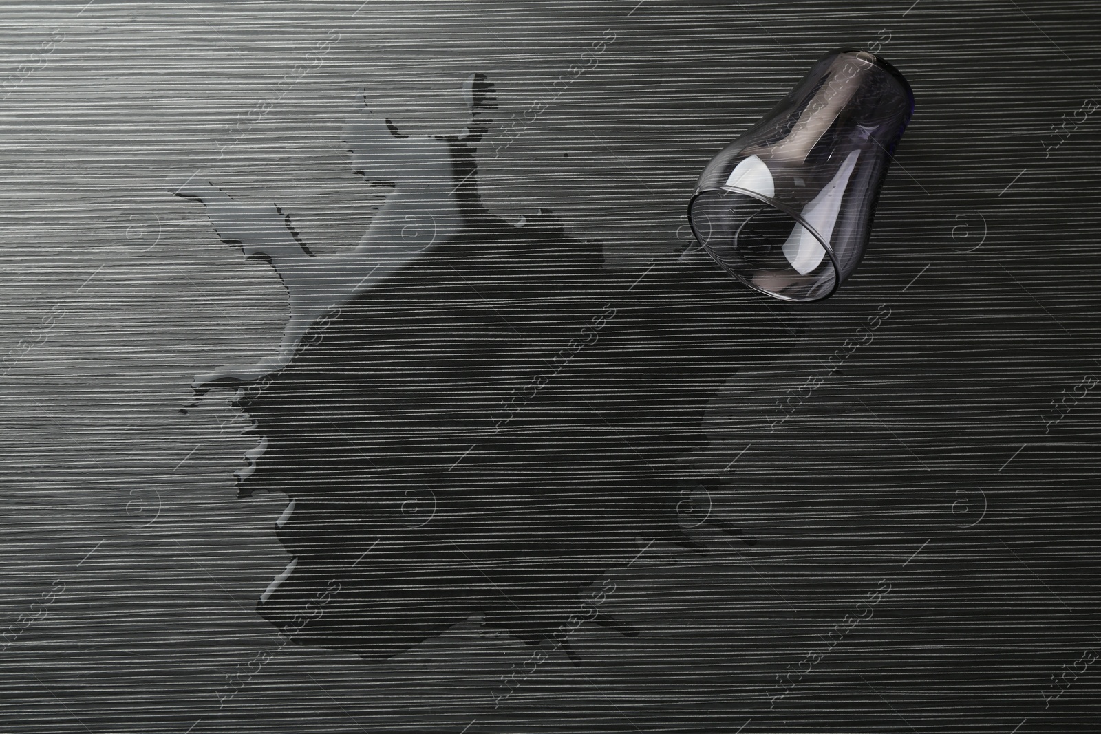 Photo of Overturned glass and spilled water on wooden table, top view