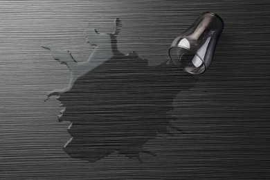 Photo of Overturned glass and spilled water on wooden table, top view