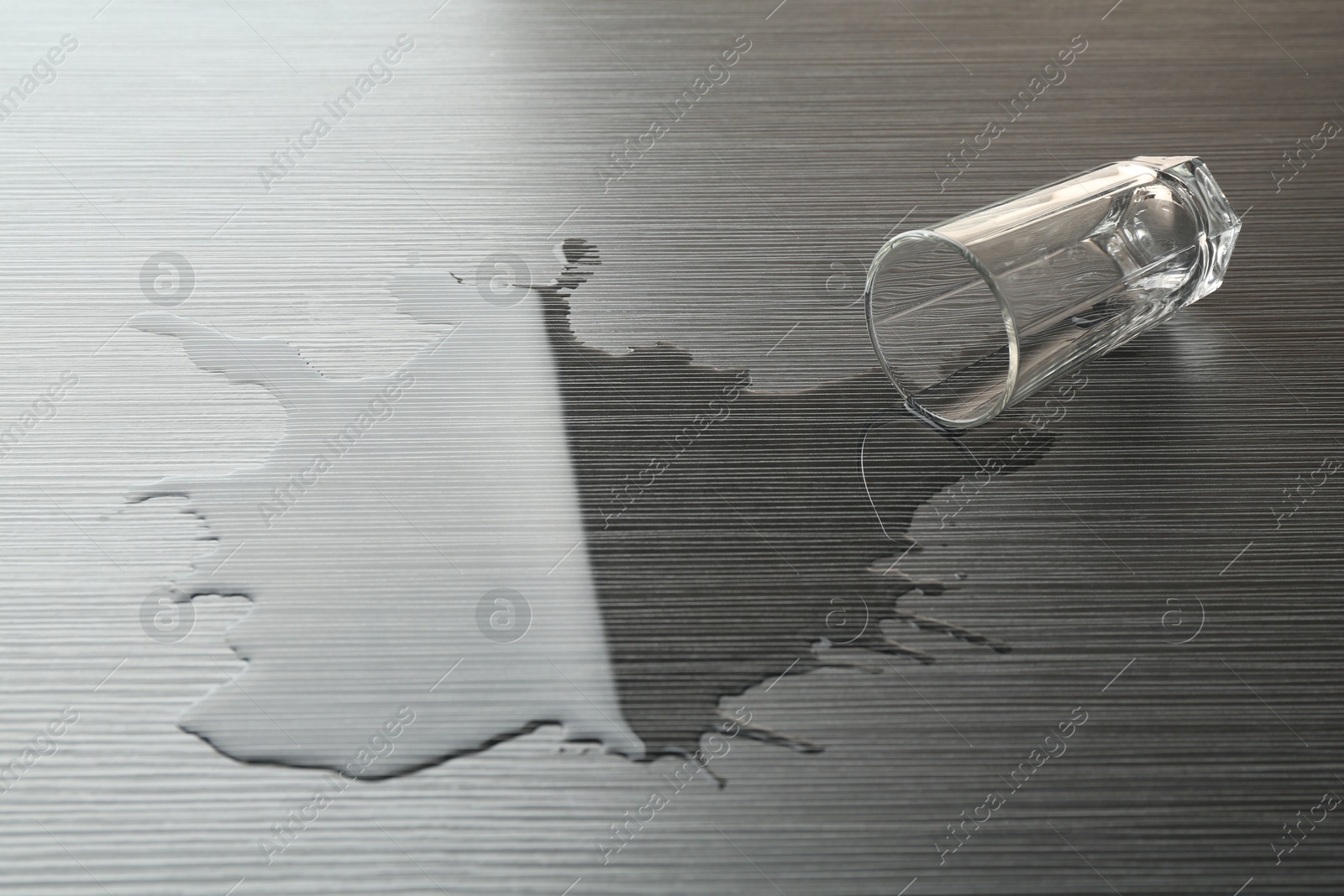 Overturned glass and spilled water on wooden table Photo of Overturned glass and spilled water on wooden table