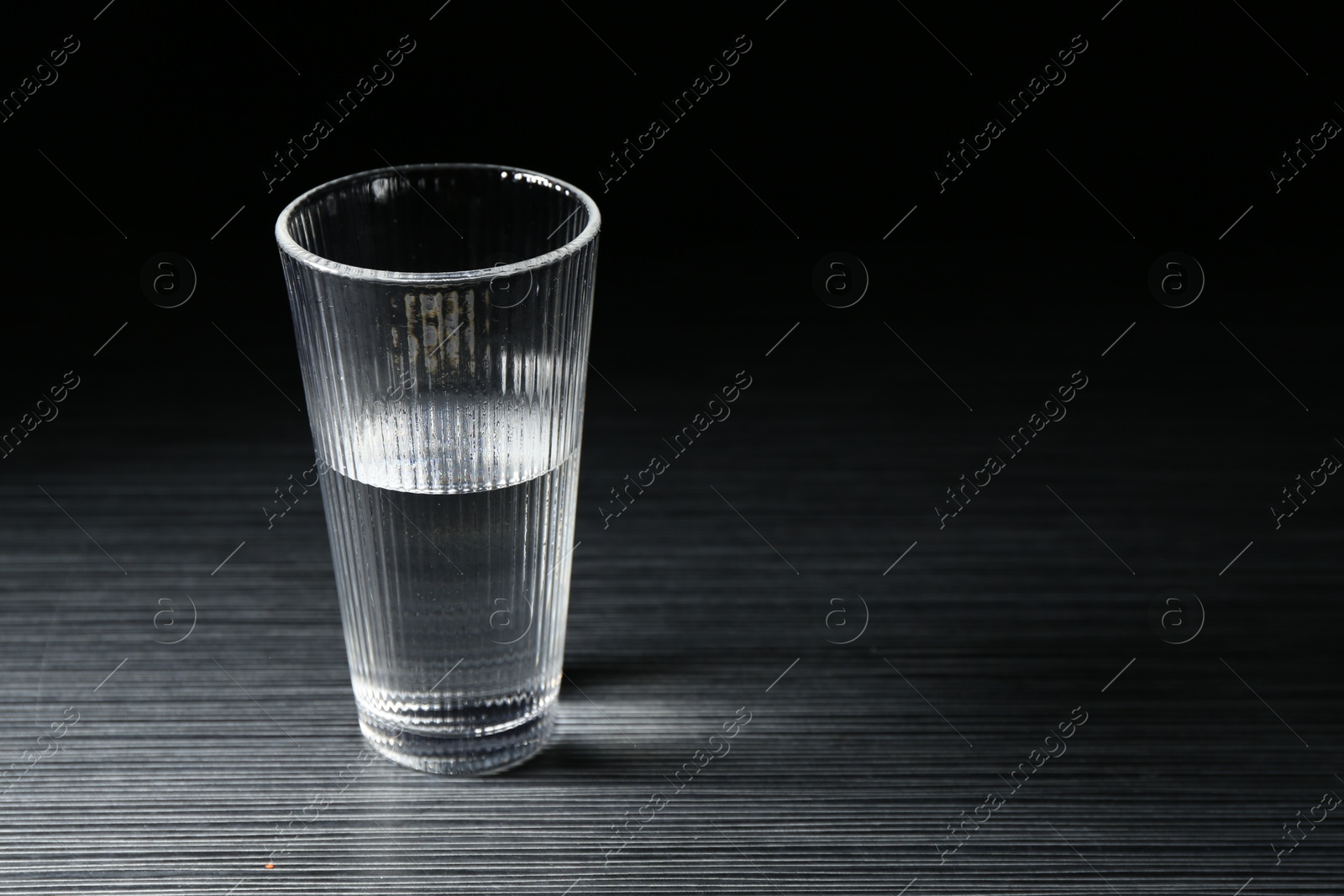 Photo of Fresh water in glass on dark wooden table, space for text