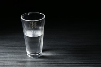 Photo of Fresh water in glass on dark wooden table, space for text