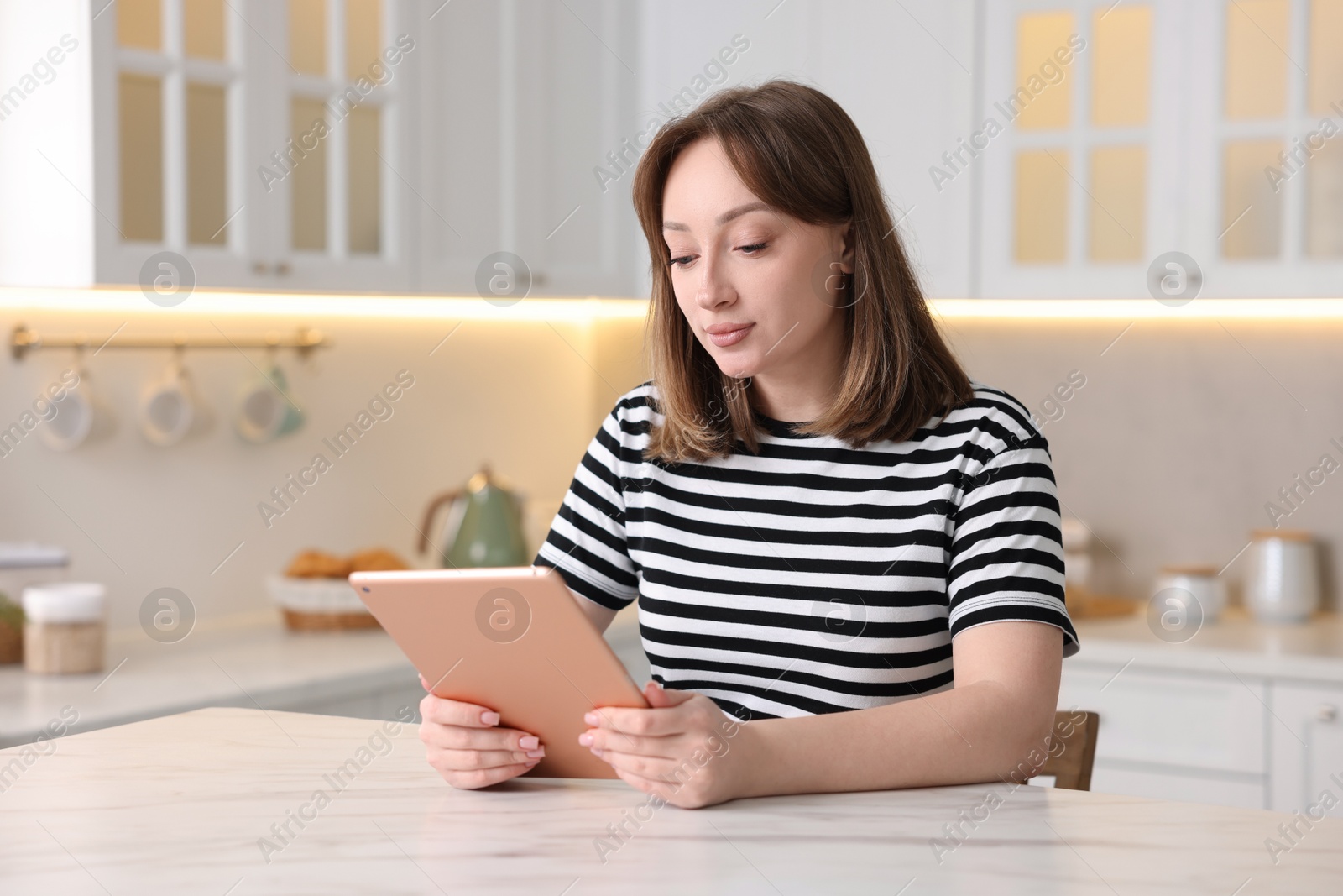 Photo of Woman with modern tablet at white marble table in kitchen