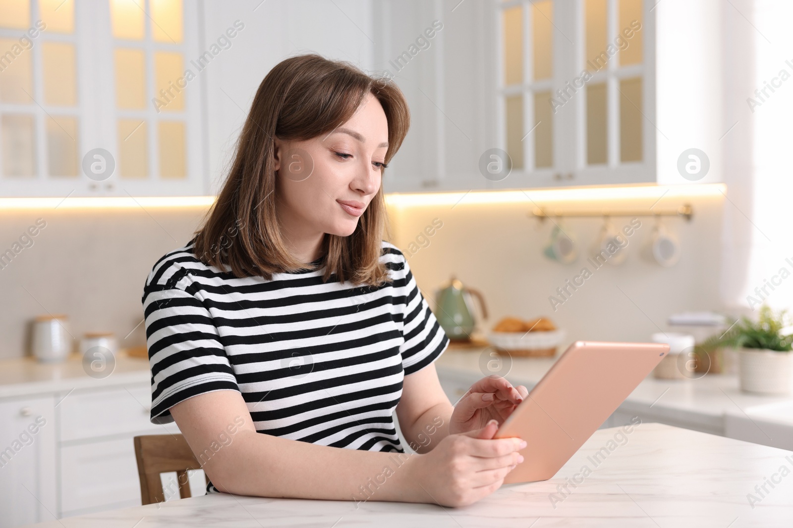 Photo of Woman with modern tablet at white marble table in kitchen
