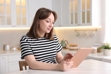 Photo of Woman with modern tablet at white marble table in kitchen