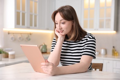 Photo of Woman with modern tablet at white marble table in kitchen