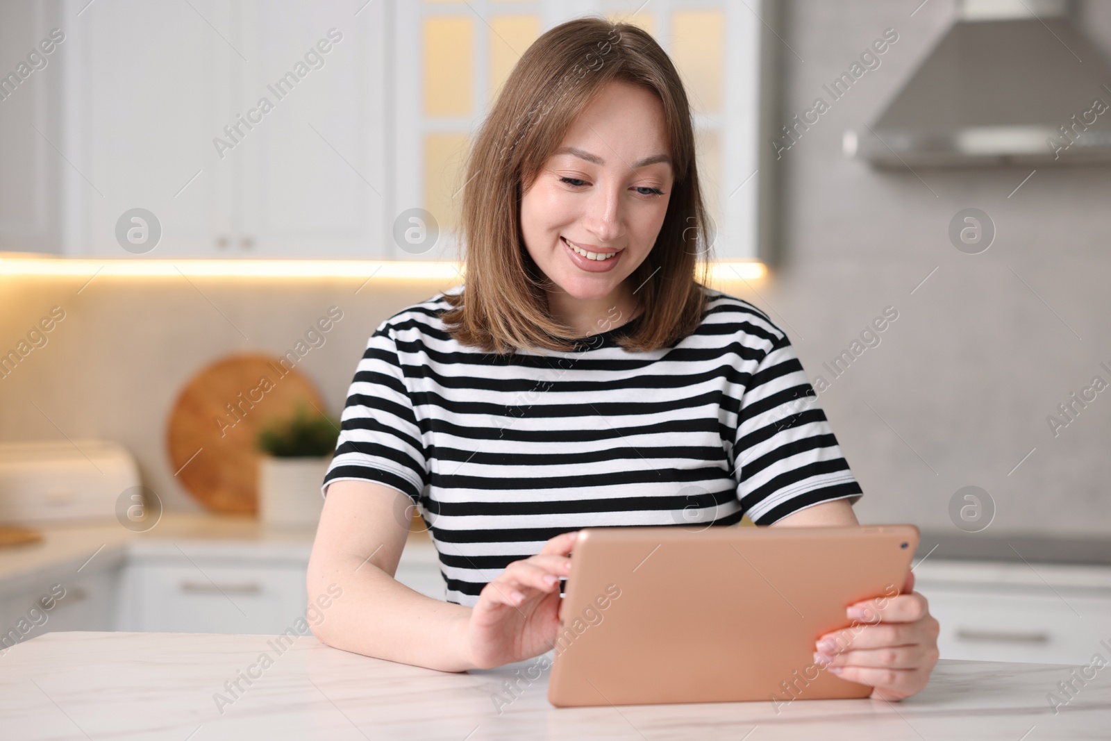Photo of Woman with modern tablet at white marble table in kitchen