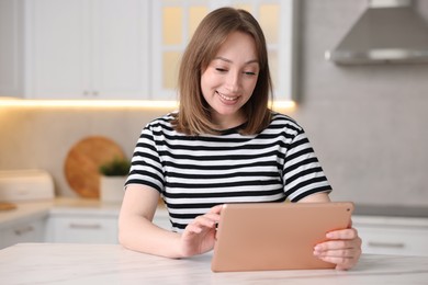Photo of Woman with modern tablet at white marble table in kitchen