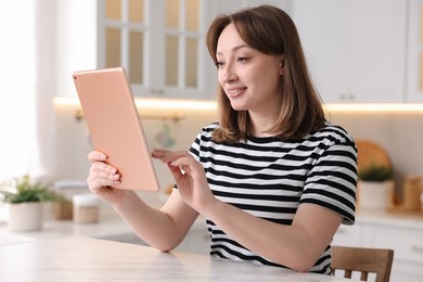Photo of Woman with modern tablet at white marble table in kitchen