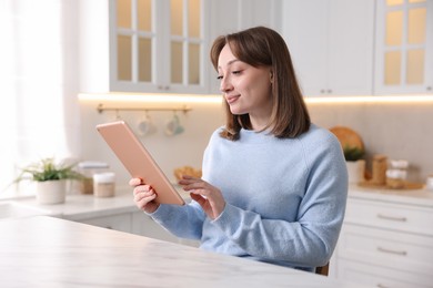 Photo of Woman with modern tablet at white marble table in kitchen