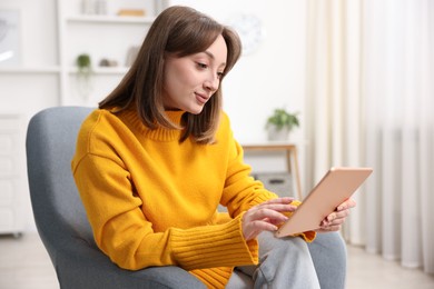 Photo of Woman with modern tablet in armchair at home