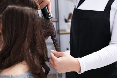 Photo of Hairdresser curling woman's hair in salon, closeup