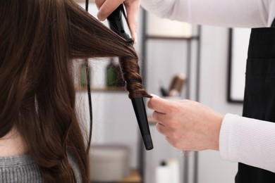 Photo of Hairdresser curling woman's hair in salon, closeup