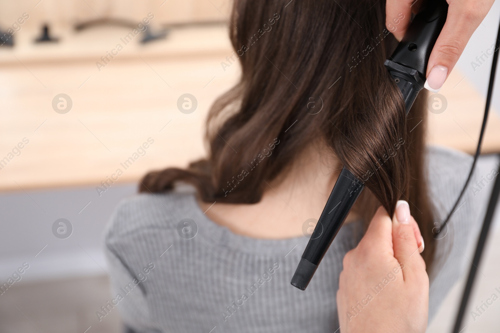Photo of Hairdresser curling woman's hair in salon, closeup. Space for text