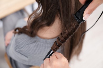 Photo of Hairdresser curling woman's hair in salon, closeup