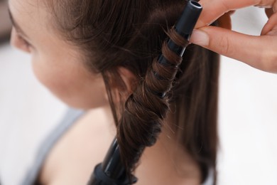 Photo of Hairdresser curling woman's hair in salon, closeup