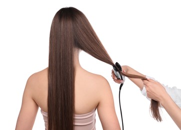 Photo of Hairdresser straightening woman's hair on white background, back view