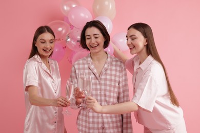 Photo of Pajama party. Happy friends with balloons clinking glasses on pink background
